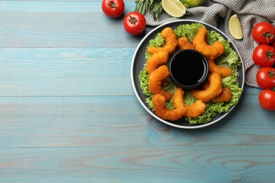 Delicious breaded fried shrimps served with sauce on light blue wooden table, top view. Space for text