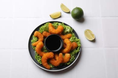 Delicious breaded fried shrimps, lime and sauce on white tiled table, top view