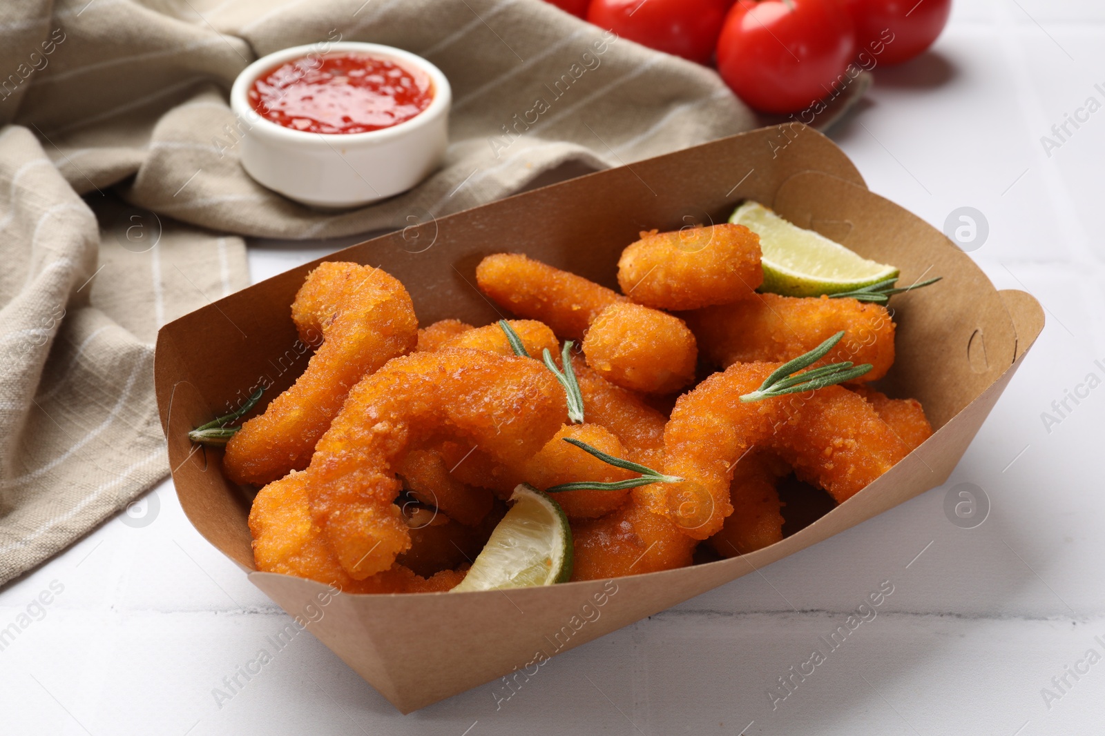 Photo of Delicious breaded fried shrimps, lime, rosemary and sauce on white table