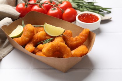 Photo of Delicious breaded fried shrimps, lime, rosemary, tomato and sauce on white table