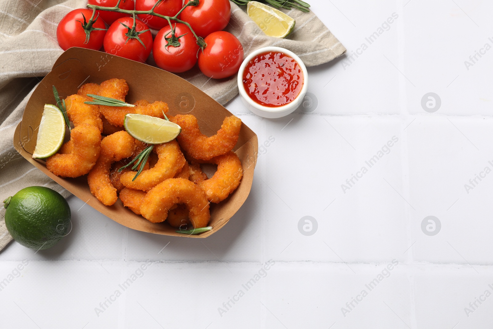 Photo of Delicious breaded fried shrimps served with lime and sauce on white tiled table, top view. Space for text