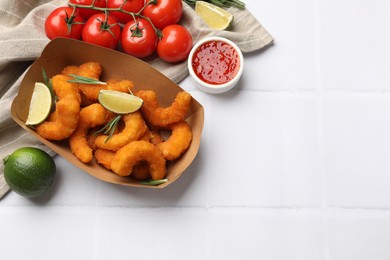 Delicious breaded fried shrimps served with lime and sauce on white tiled table, top view. Space for text