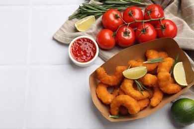 Photo of Delicious breaded fried shrimps served with lime and sauce on white tiled table, top view. Space for text