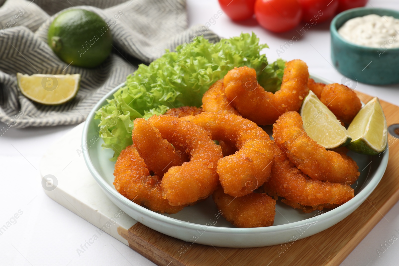 Photo of Delicious breaded fried shrimps, lime and lettuce on white table