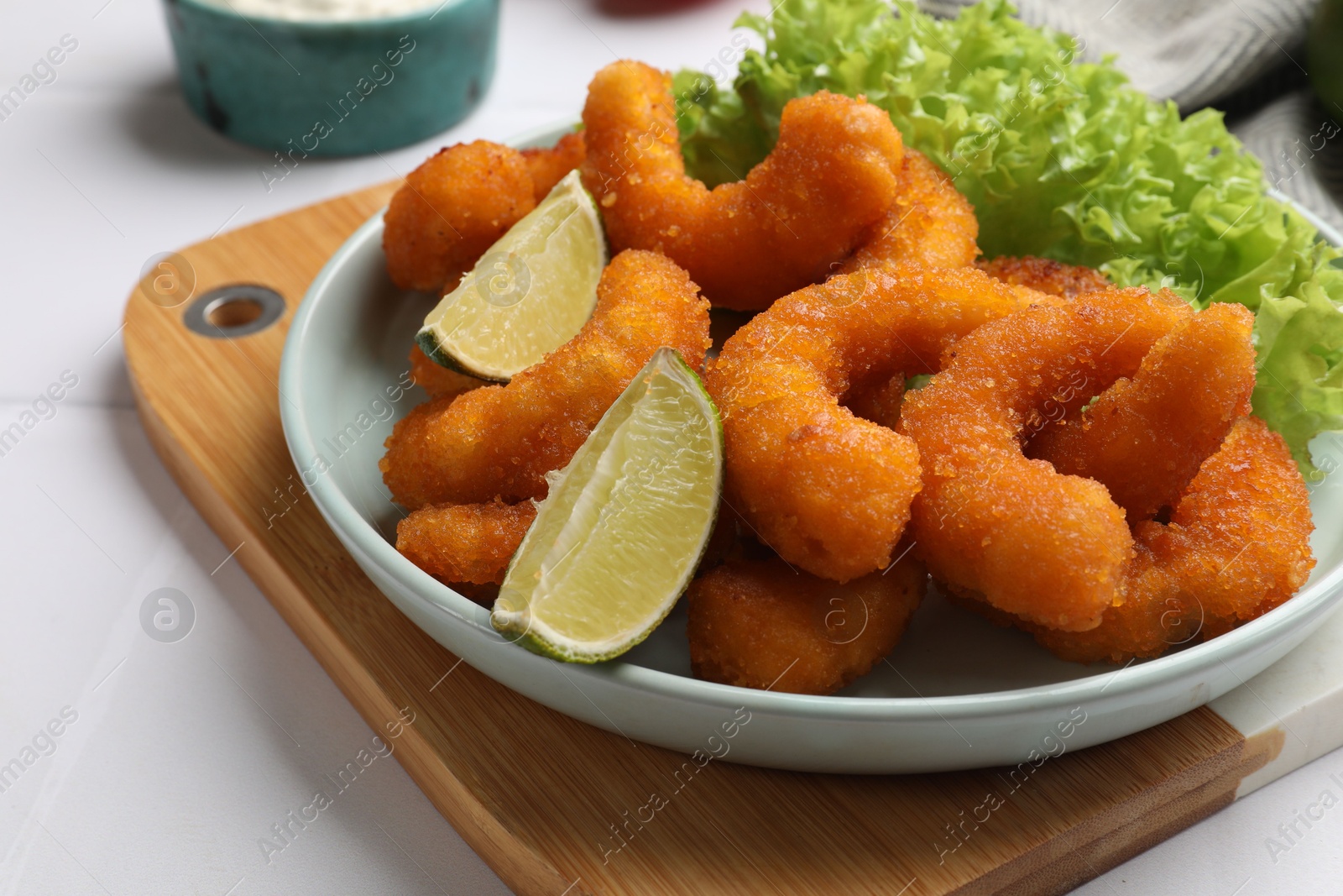 Photo of Delicious breaded fried shrimps, lime and lettuce on white table, closeup