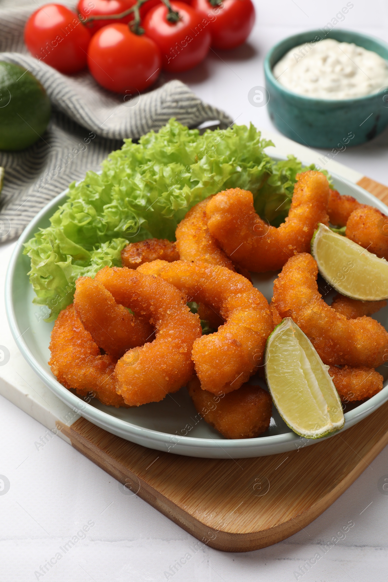 Photo of Delicious breaded fried shrimps, lime and lettuce on white table