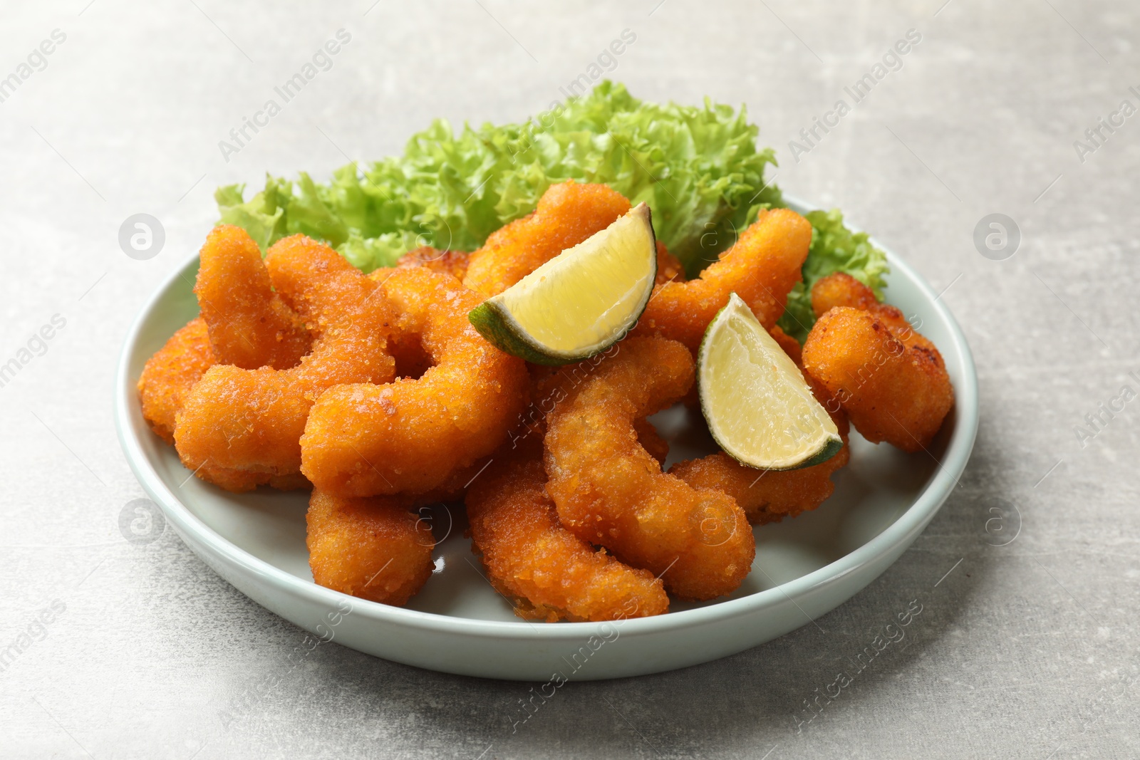 Photo of Delicious breaded fried shrimps, lime and lettuce on light grey table