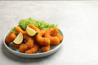 Photo of Delicious breaded fried shrimps, lime and lettuce on light grey table, space for text