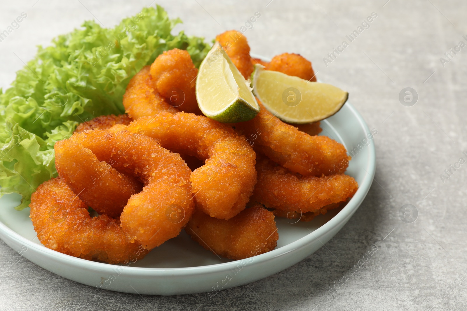 Photo of Delicious breaded fried shrimps, lime and lettuce on light grey table, closeup