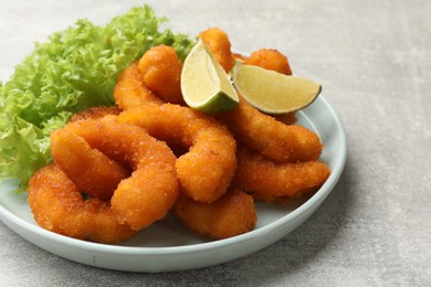 Delicious breaded fried shrimps, lime and lettuce on light grey table, closeup