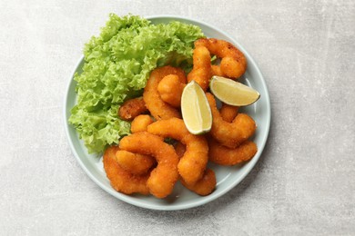 Delicious breaded fried shrimps, lime and lettuce on light grey table, top view