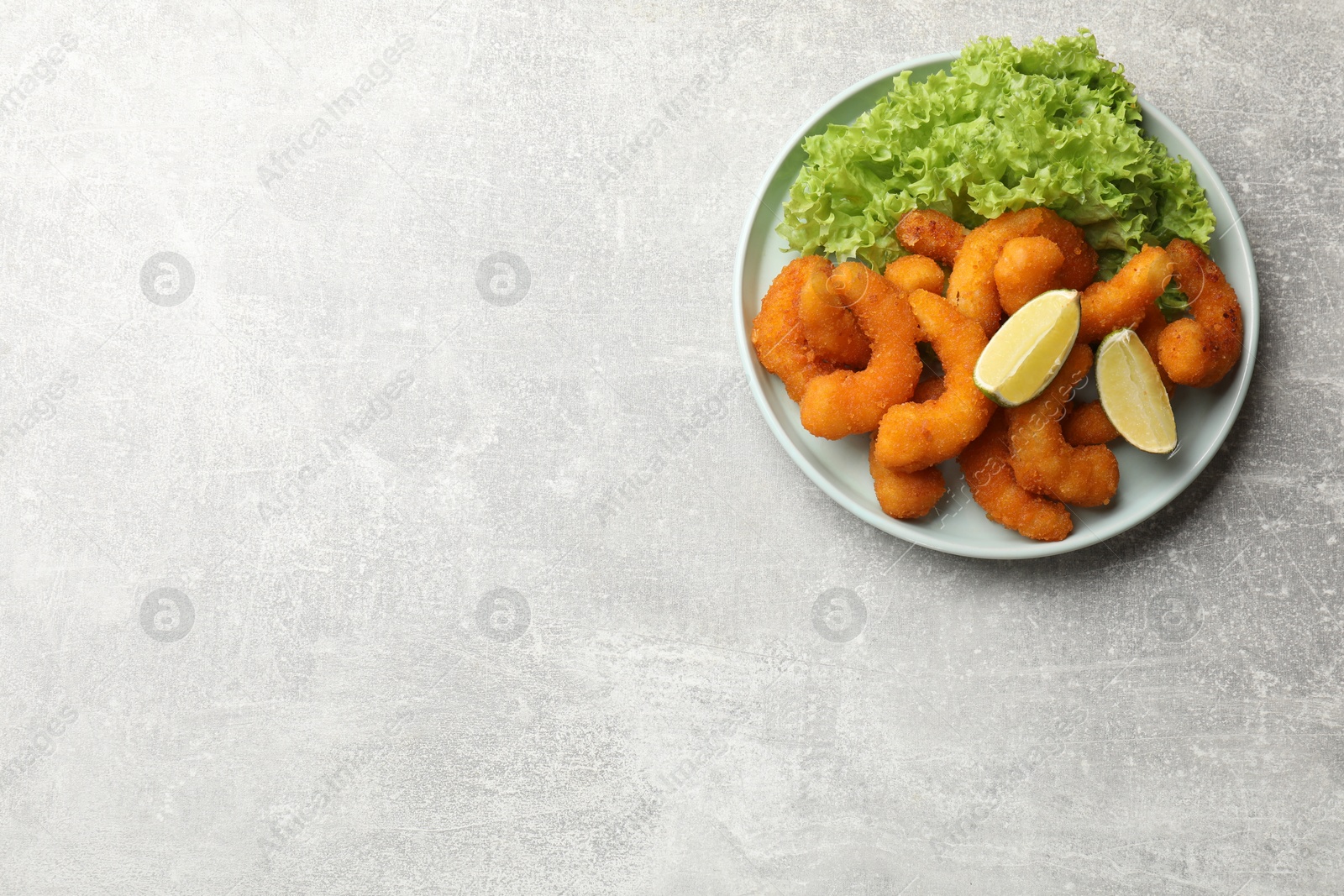 Photo of Delicious breaded fried shrimps, lime and lettuce on light grey table, top view. Space for text