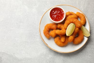 Delicious breaded fried shrimps, lime and sauce on light grey table, top view. Space for text