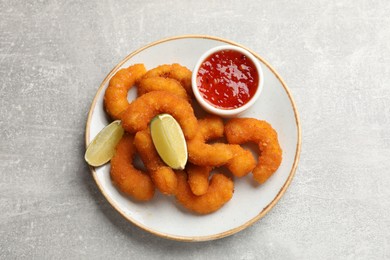 Delicious breaded fried shrimps, lime and sauce on light grey table, top view