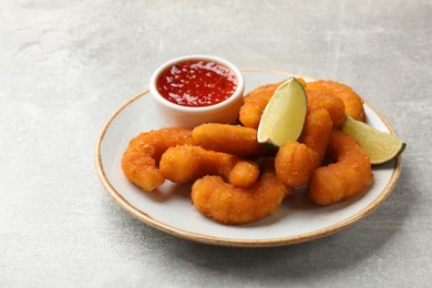 Delicious breaded fried shrimps, lime and sauce on light grey table