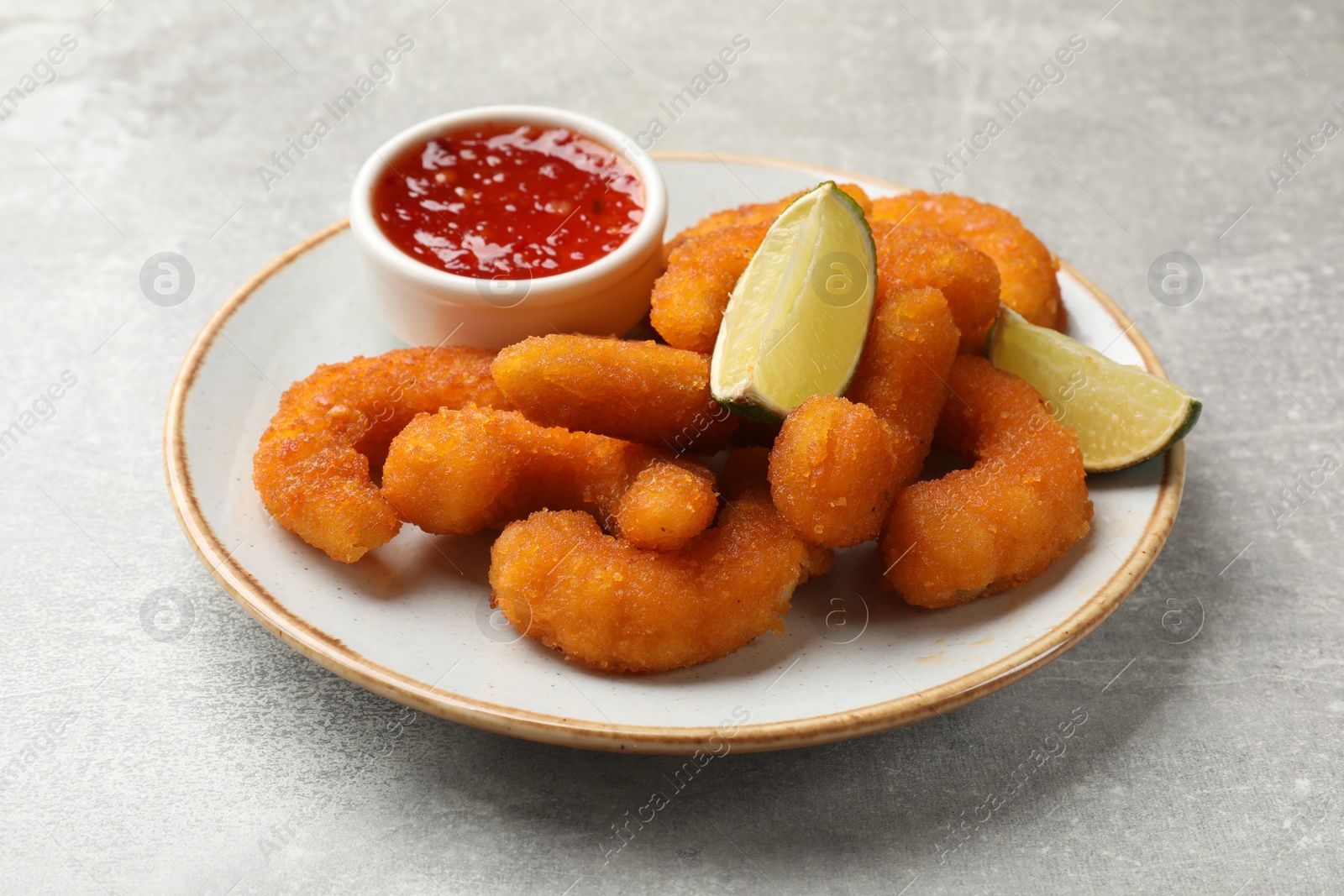 Photo of Delicious breaded fried shrimps, lime and sauce on light grey table