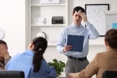 Man with clipboard feeling embarrassed during business meeting in office