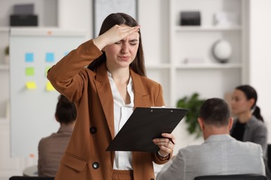 Woman with clipboard feeling embarrassed during business meeting in office