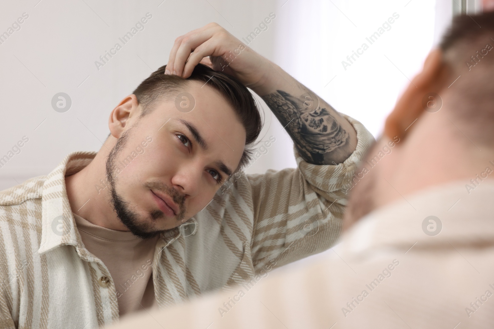 Photo of Baldness concept. Sad man with receding hairline looking at mirror indoors