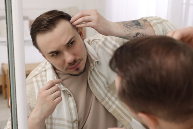 Photo of Baldness concept. Sad man with receding hairline looking at mirror indoors