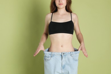 Photo of Woman in big jeans showing her slim body on olive background, closeup