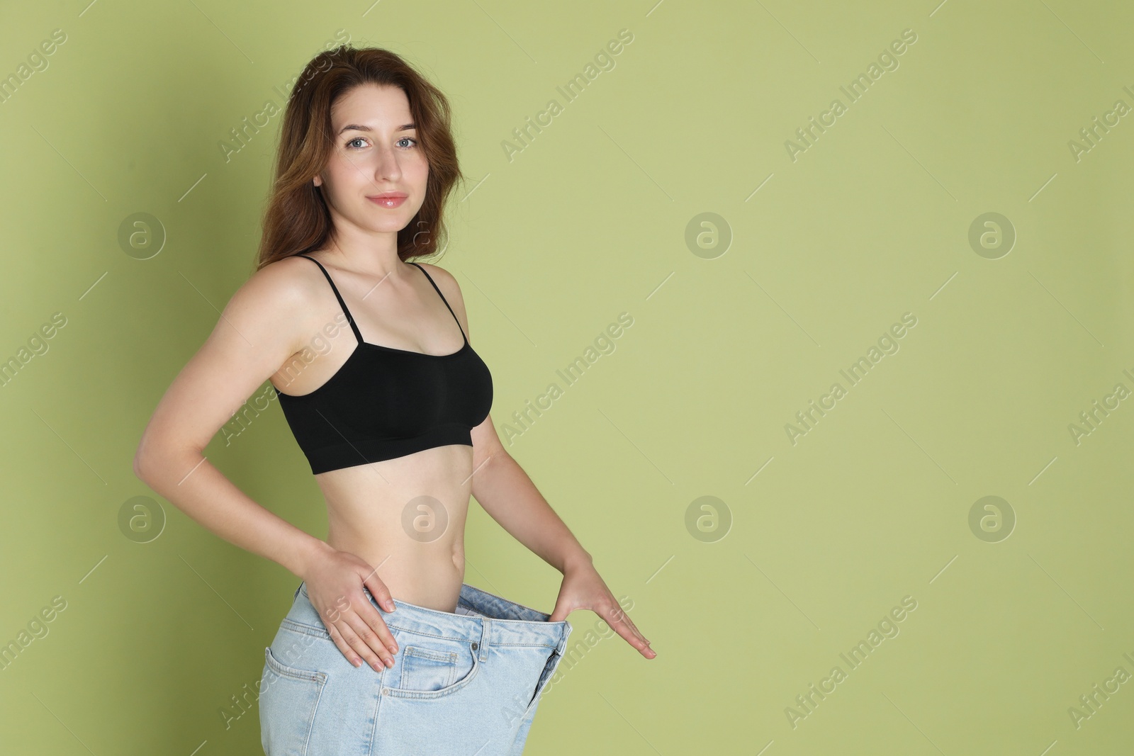 Photo of Woman in big jeans showing her slim body on olive background, space for text