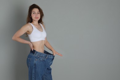 Photo of Woman in big jeans showing her slim body on grey background, space for text