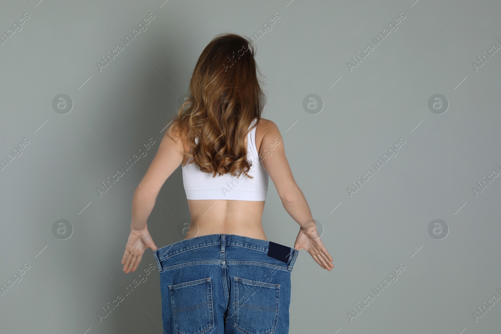 Photo of Woman in big jeans showing her slim body on grey background, back view