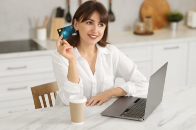 Online banking. Smiling woman with credit card and laptop paying purchase at table indoors