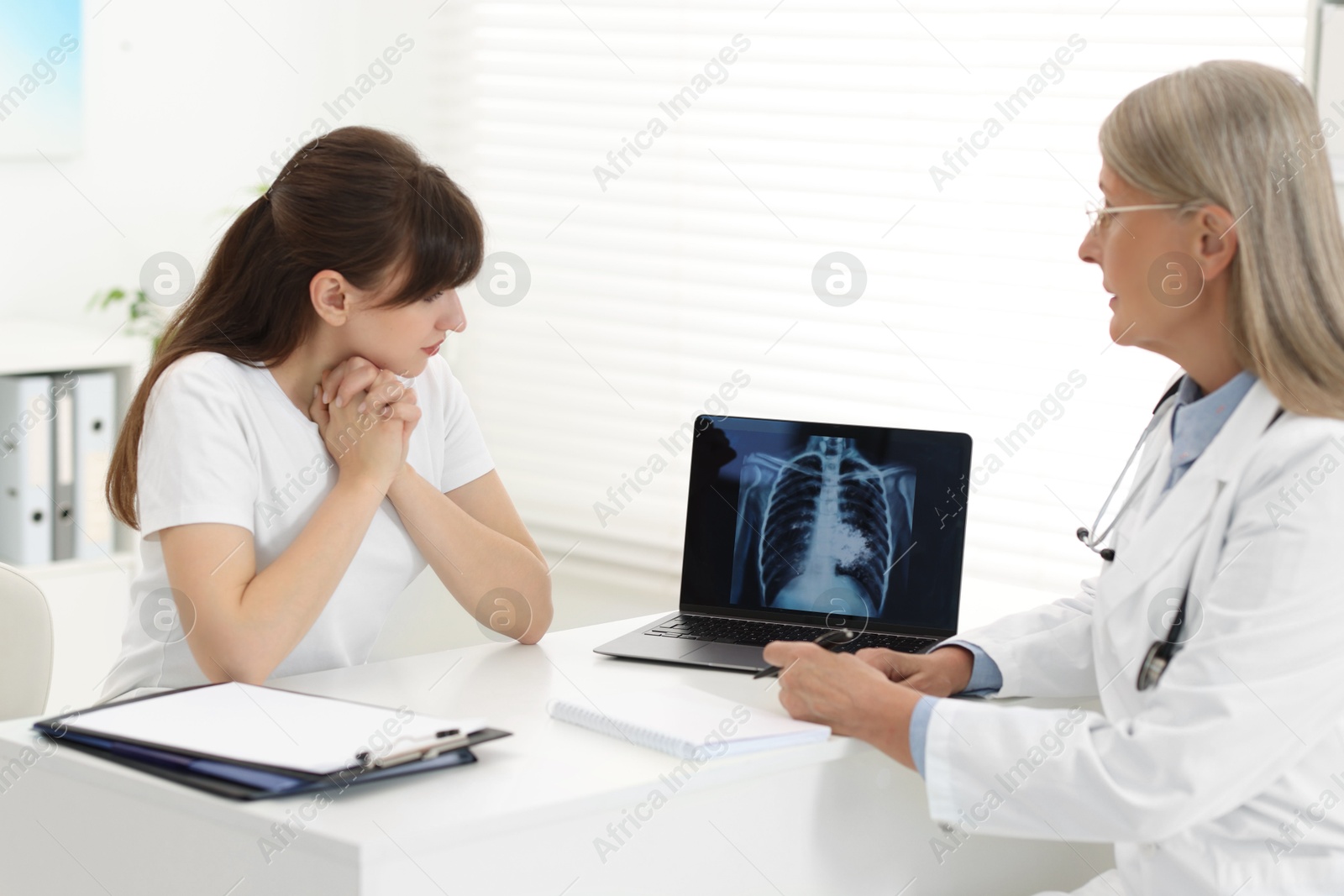 Photo of Lung cancer. Doctor showing chest x-ray on laptop to her patient in clinic