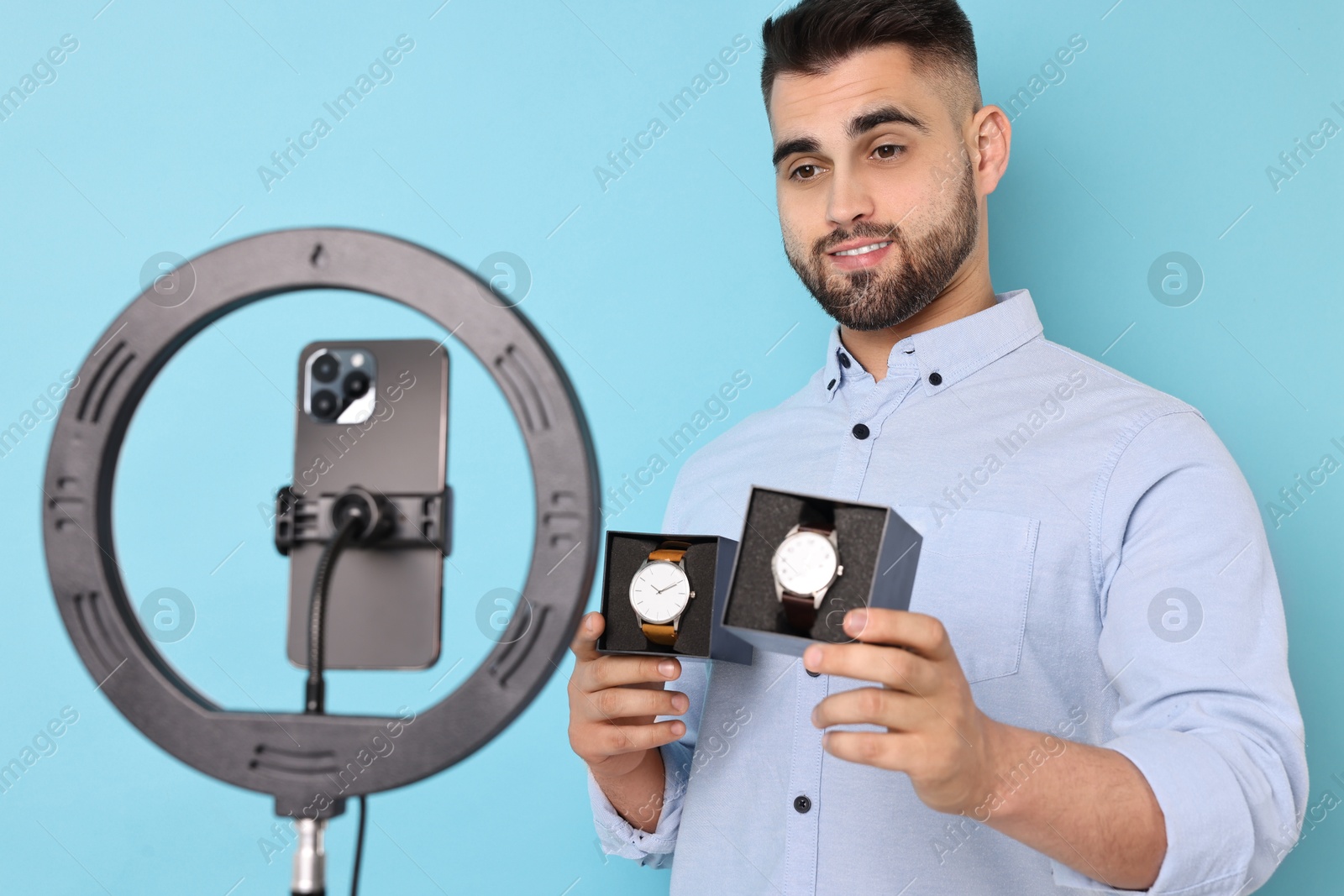 Photo of Fashion blogger reviewing watches and recording video with smartphone and ring lamp on light blue background