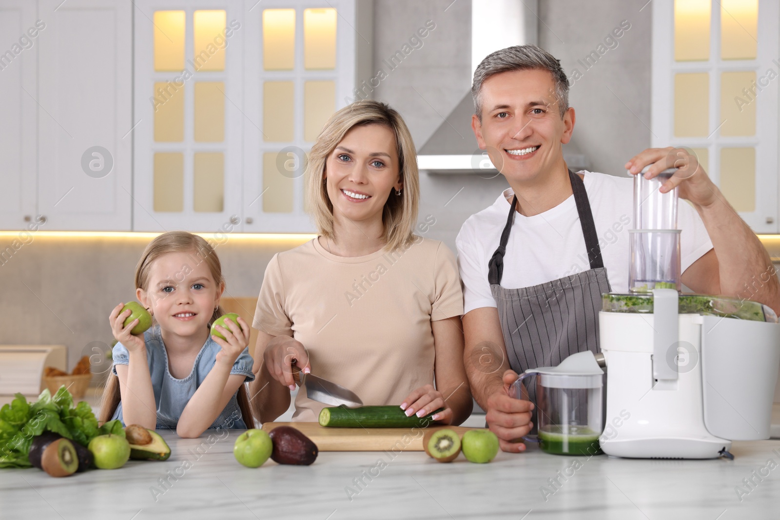 Photo of Happy family with juicer and fresh products making drink at white marble table in kitchen