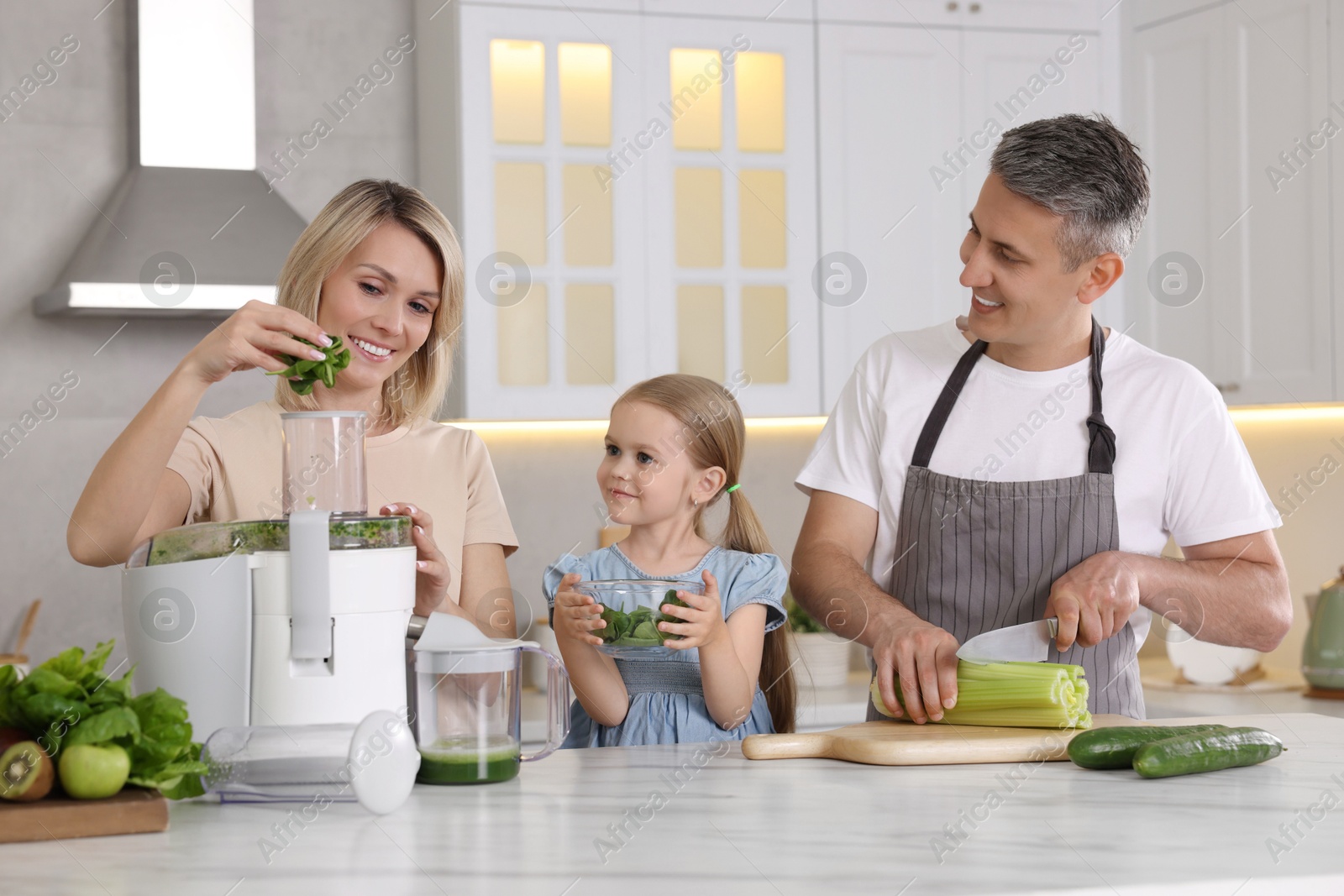 Photo of Happy family with juicer and fresh products making drink at white marble table in kitchen