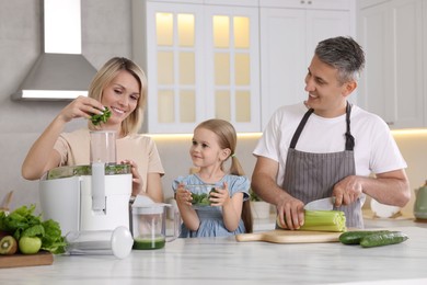 Happy family with juicer and fresh products making drink at white marble table in kitchen