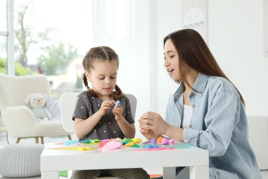 Mother and her daughter sculpting with play dough at table indoors