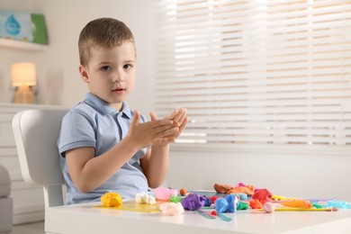 Photo of Little boy sculpting with play dough at table indoors