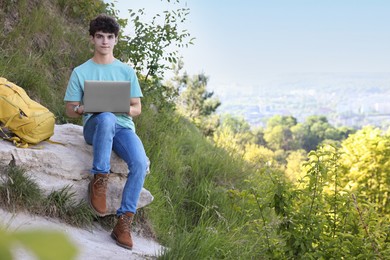 Photo of Travel blogger using laptop on stone outdoors, space for text