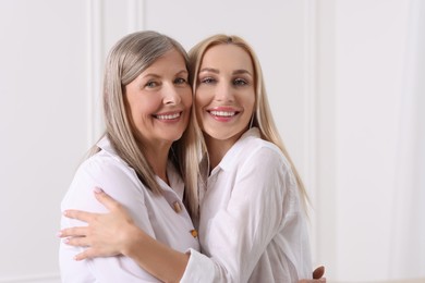 Family portrait of young woman and her mother near white wall