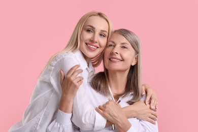 Family portrait of young woman and her mother on pink background