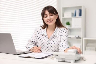 Smiling secretary taking telephone handset at table in office