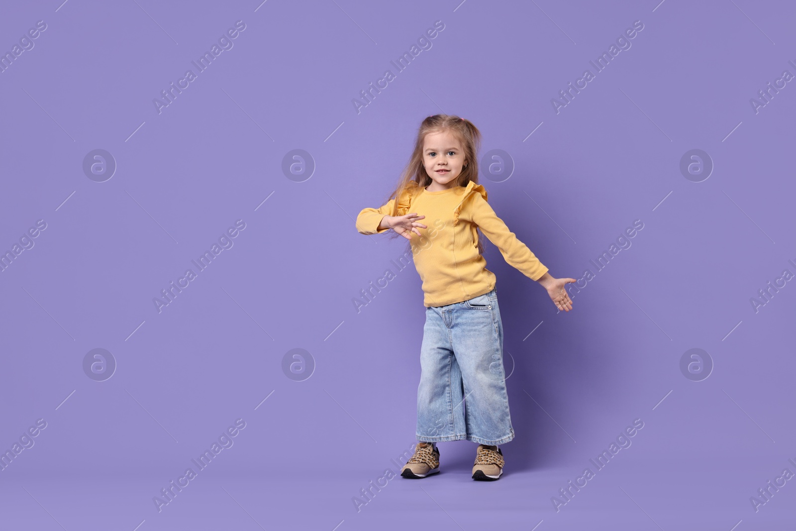 Photo of Cute little girl dancing on purple background, space for text