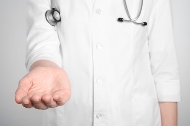 Doctor holding something on light grey background, closeup