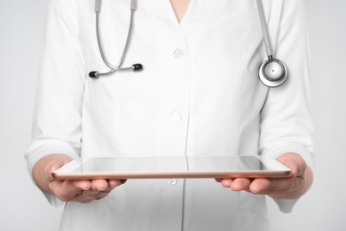 Doctor with tablet on light grey background, closeup