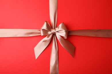 Beige satin ribbon with bow on red background, top view