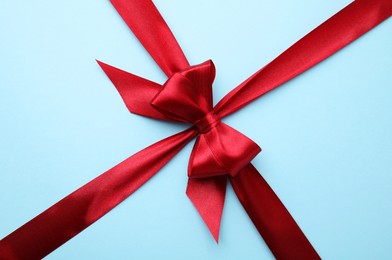 Red satin ribbon with bow on light blue background, top view