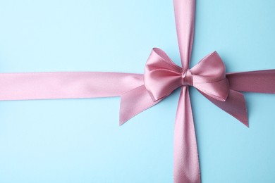 Pink satin ribbon with bow on light blue background, top view