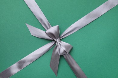 Grey satin ribbon with bow on green background, top view