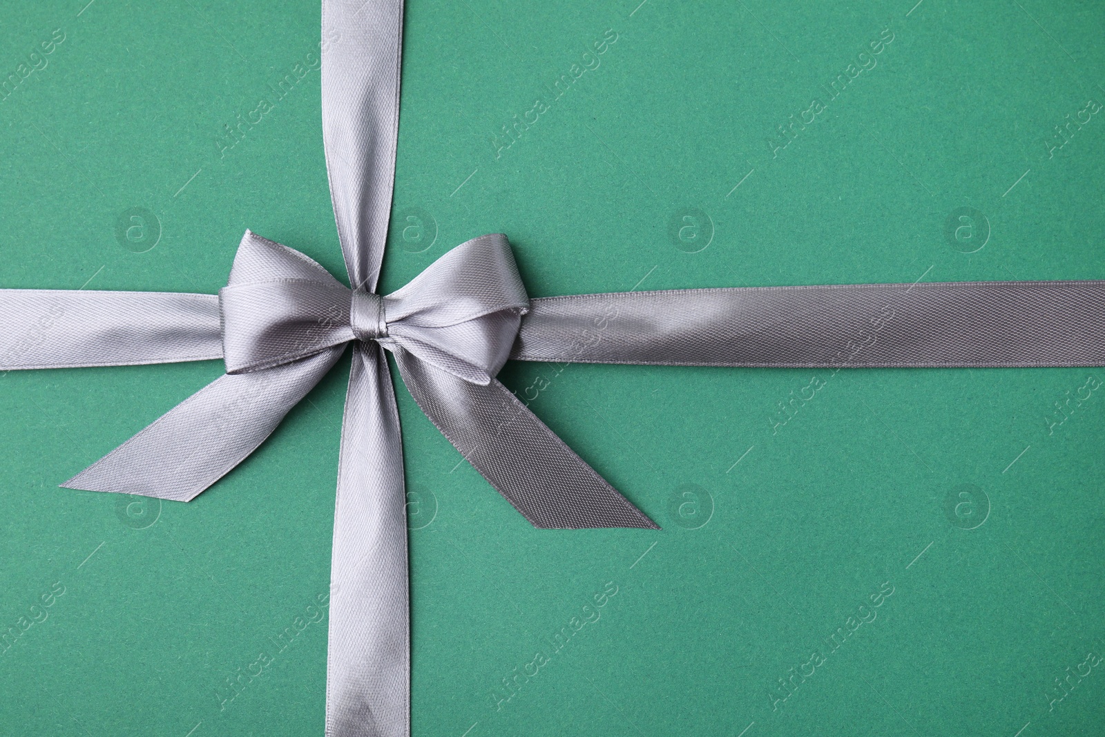 Photo of Grey satin ribbon with bow on green background, top view