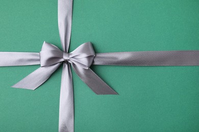 Grey satin ribbon with bow on green background, top view