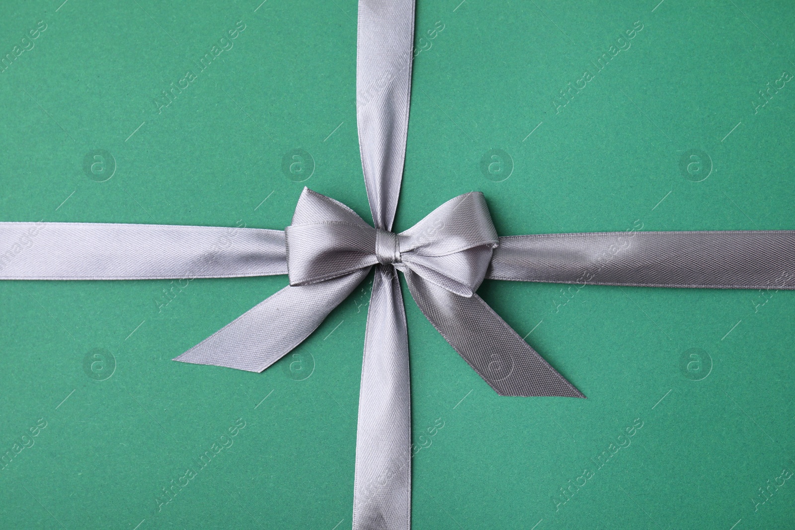 Photo of Grey satin ribbon with bow on green background, top view